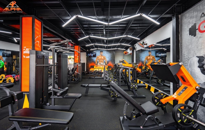 Alpha Fitness and Yoga Center gym floor with orange and black machines, benches and wall murals