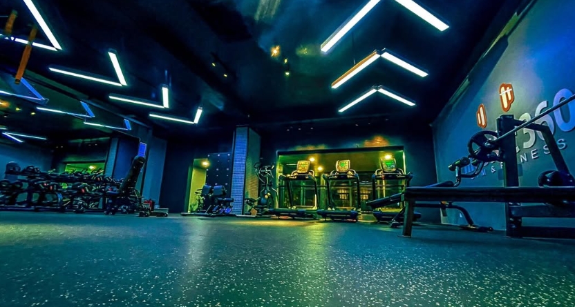Modern gym with blue and green neon lighting, cardio machines and a row of treadmills in the dark