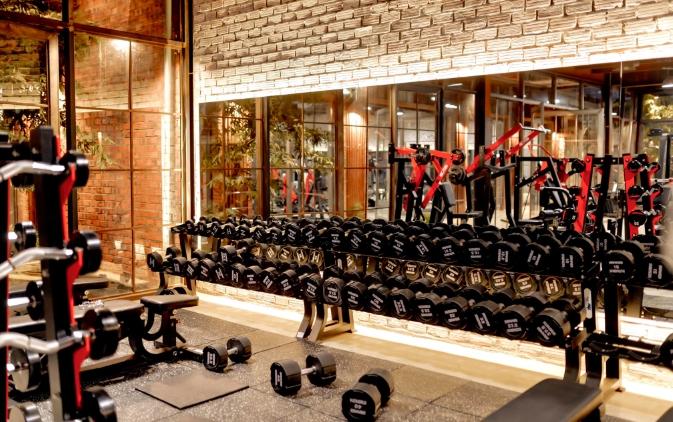 Long rack of black dumbbells and weight equipment in a gym with brick walls and large windows