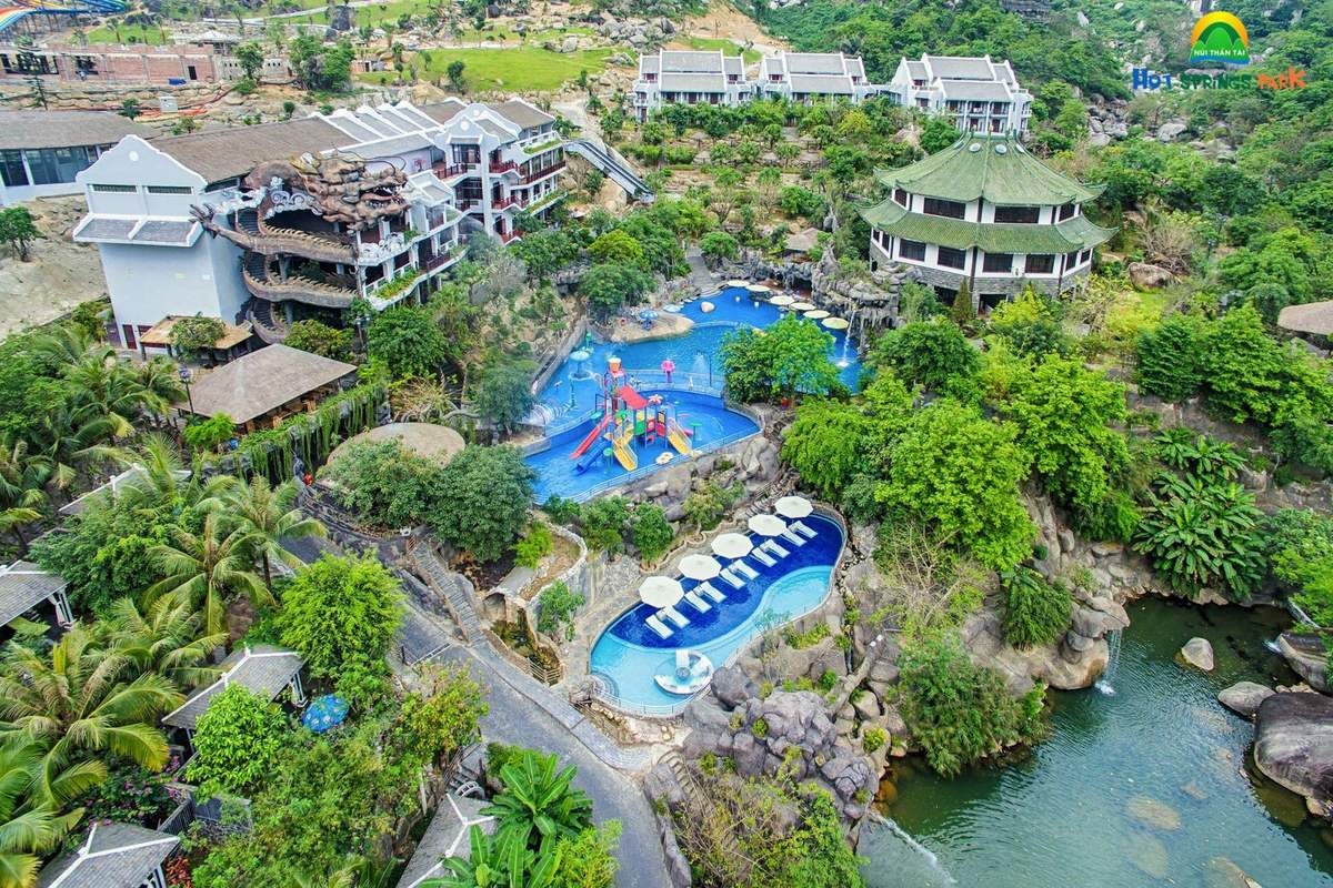 Aerial view of a hillside hot springs water park with blue pools, slides and parasols among lush greenery