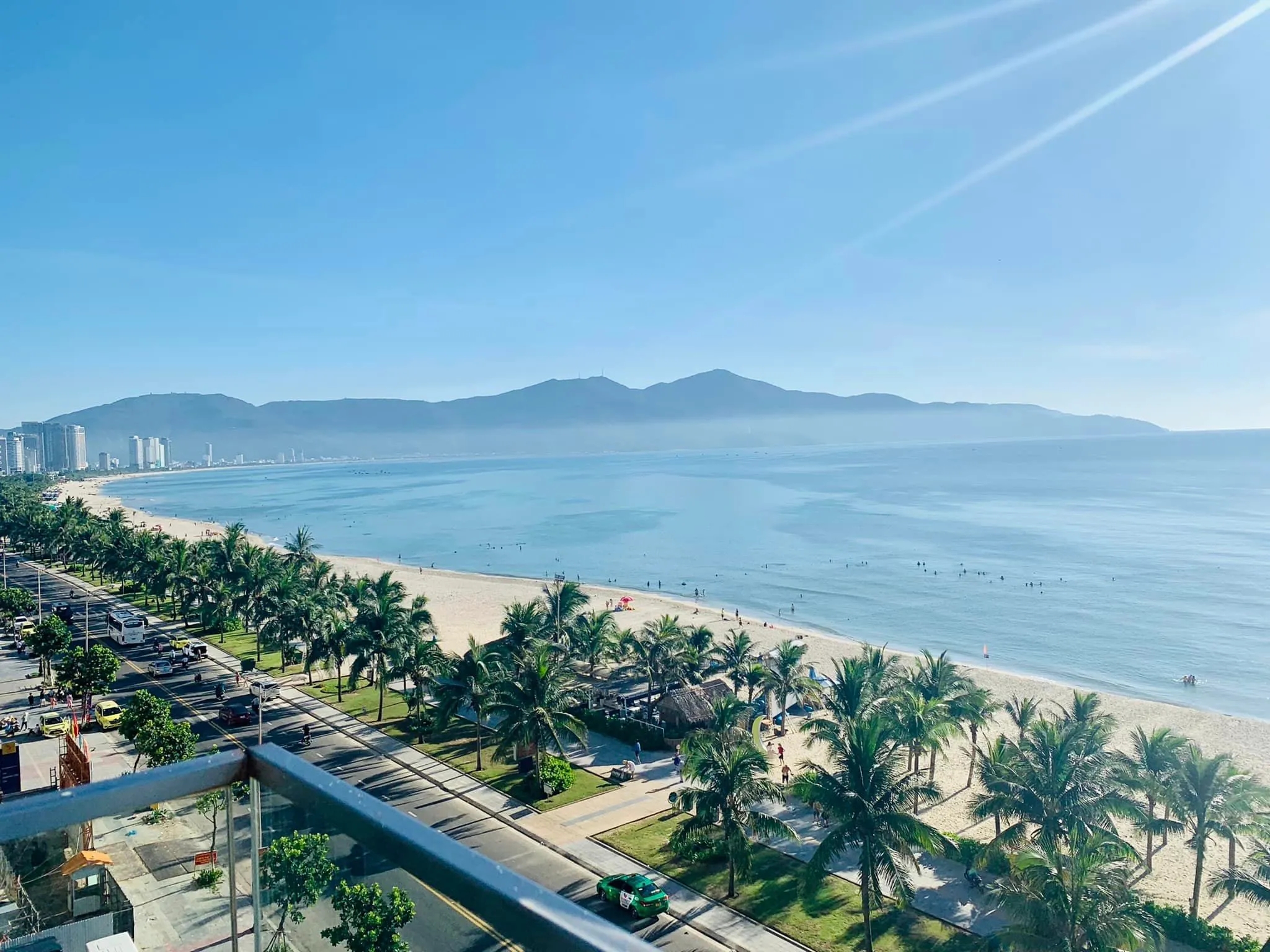Elevated view of My Khe Beach with a palm-lined coastal road, white sand and mountains across the bay