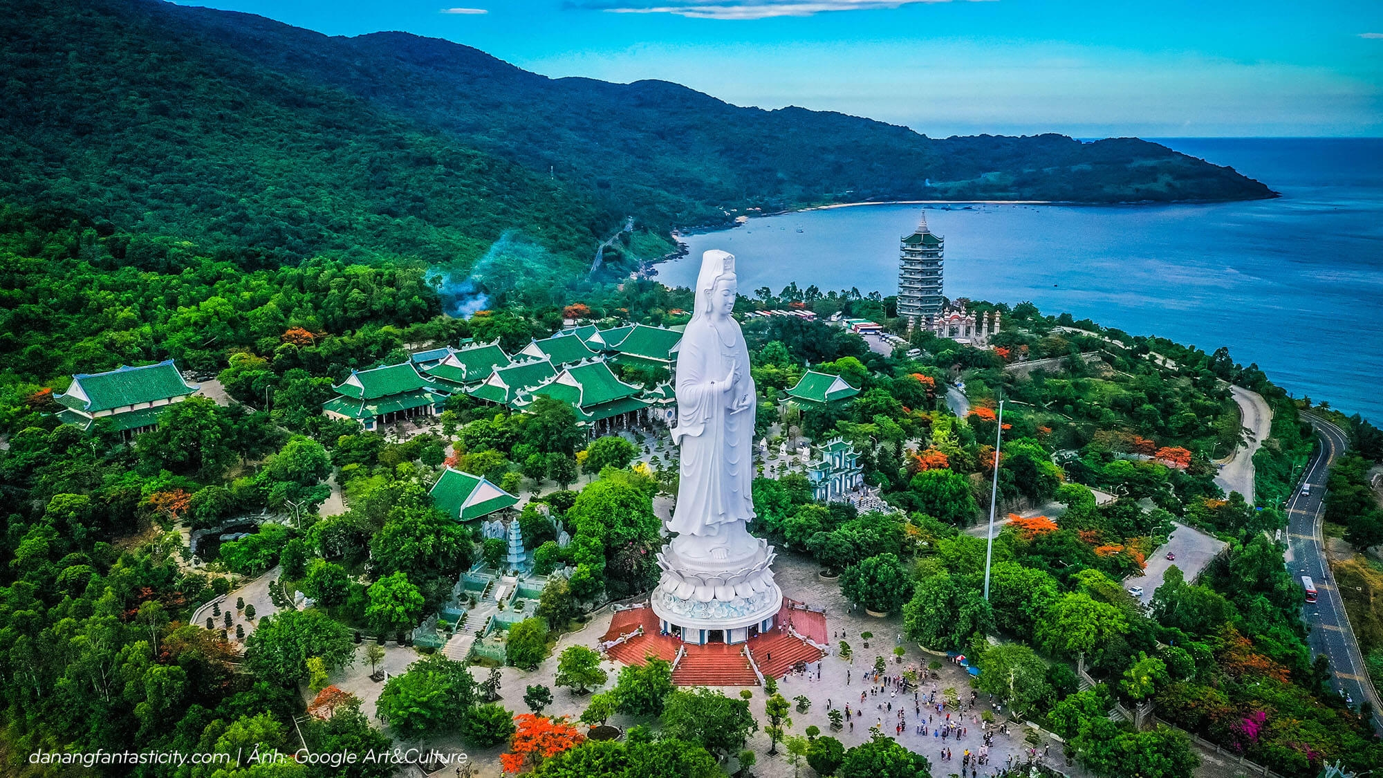 Aerial view of the white Lady Buddha statue at Linh Ung Pagoda among green hills above the coast in Da Nang