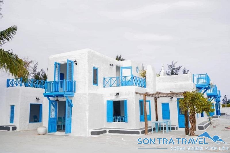 Whitewashed Greek-style buildings with bright blue doors, shutters and balconies beside a palm tree