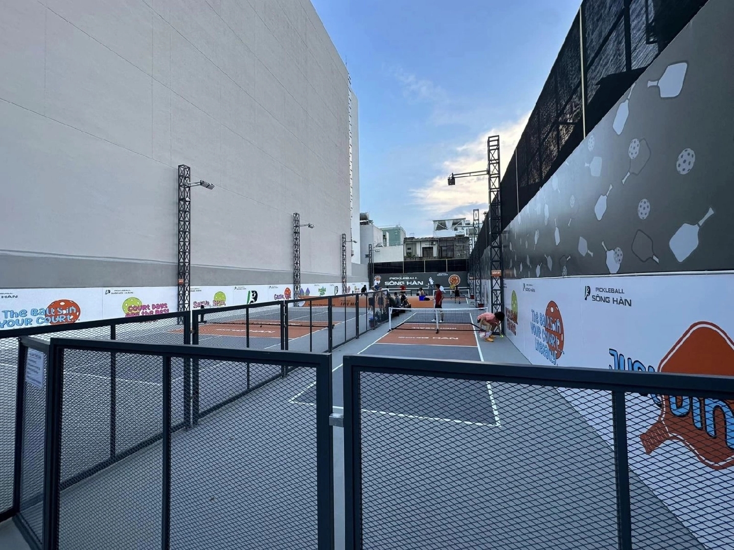 Rooftop Song Han pickleball venue with several outdoor courts ringed by branded fencing and tall city walls