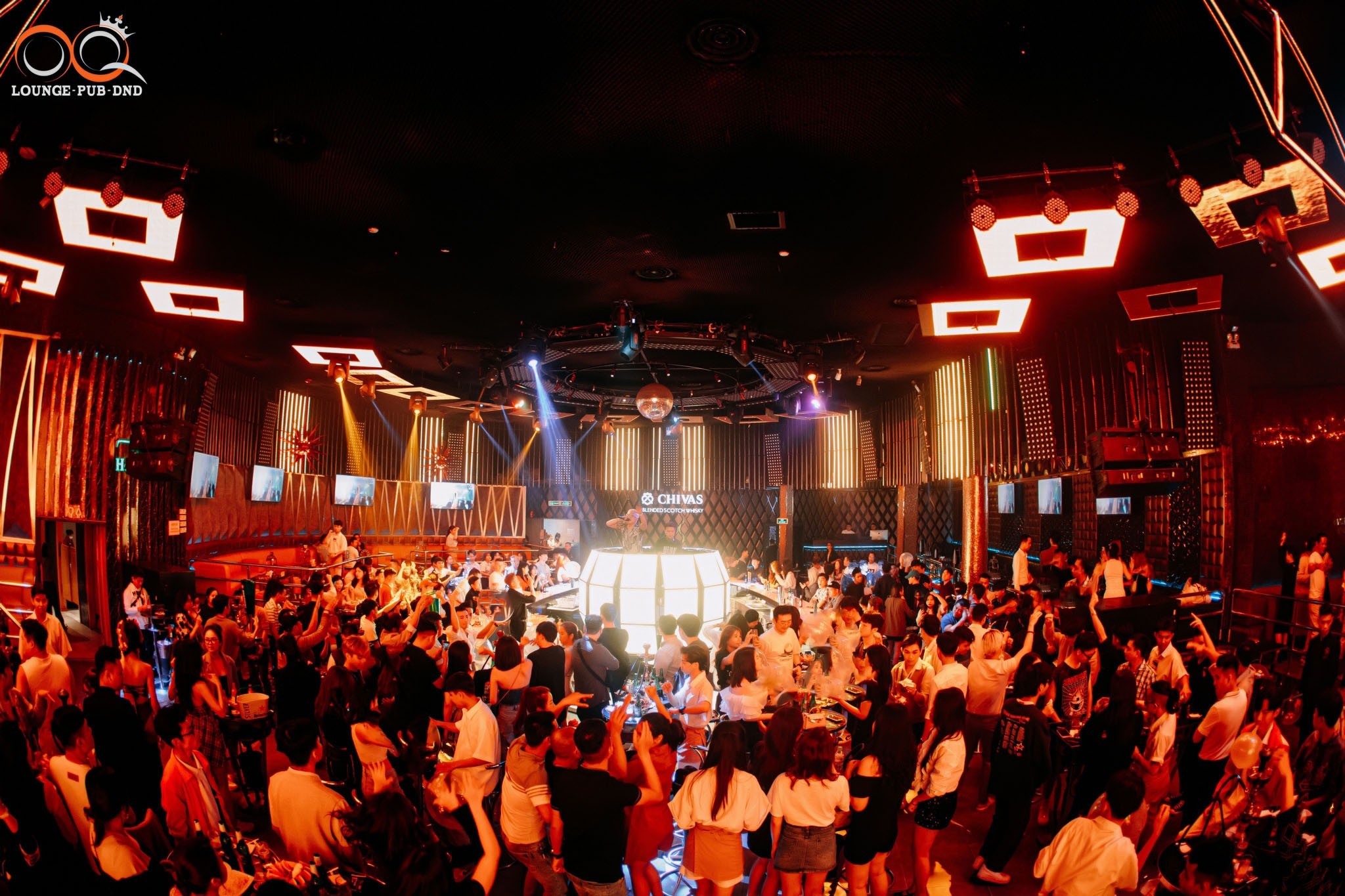 OQ Lounge Pub DnD interior glowing in warm orange light with a busy crowd around the dance floor