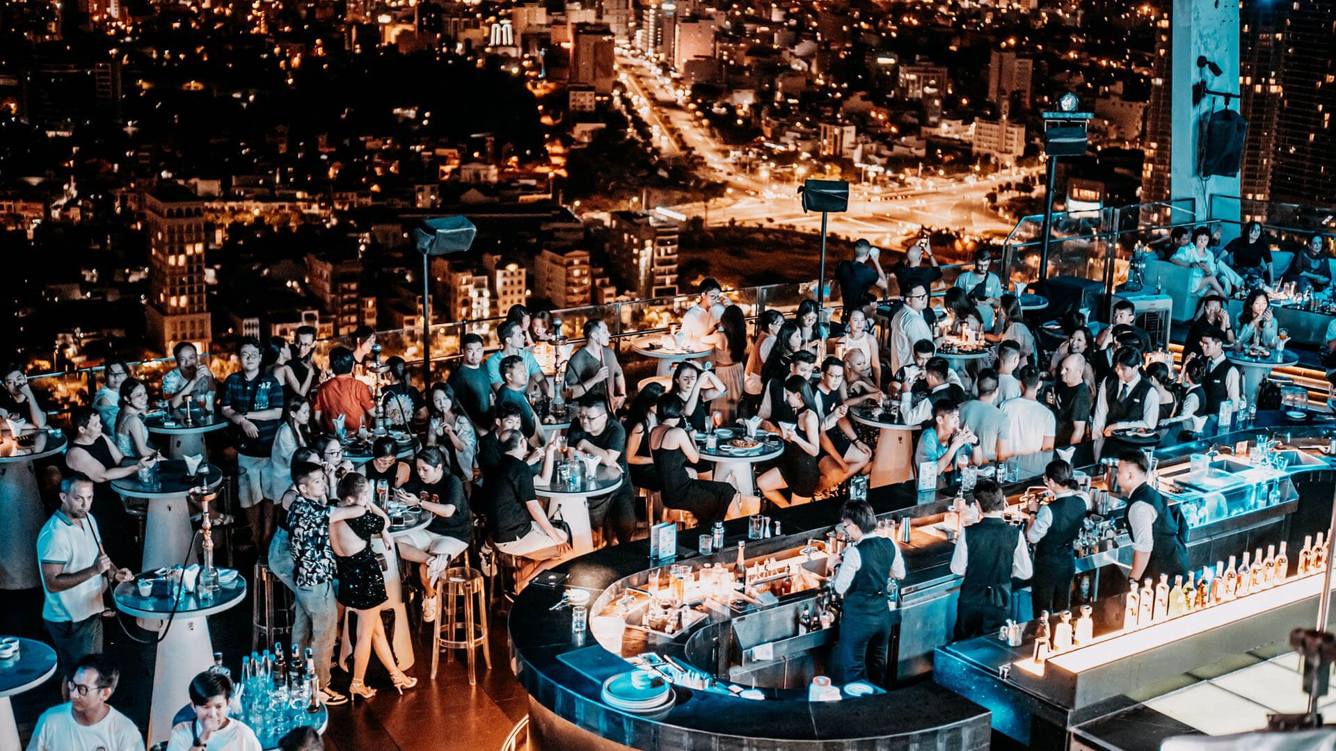 Crowded rooftop bar with a curved counter overlooking the glittering Da Nang city skyline at night