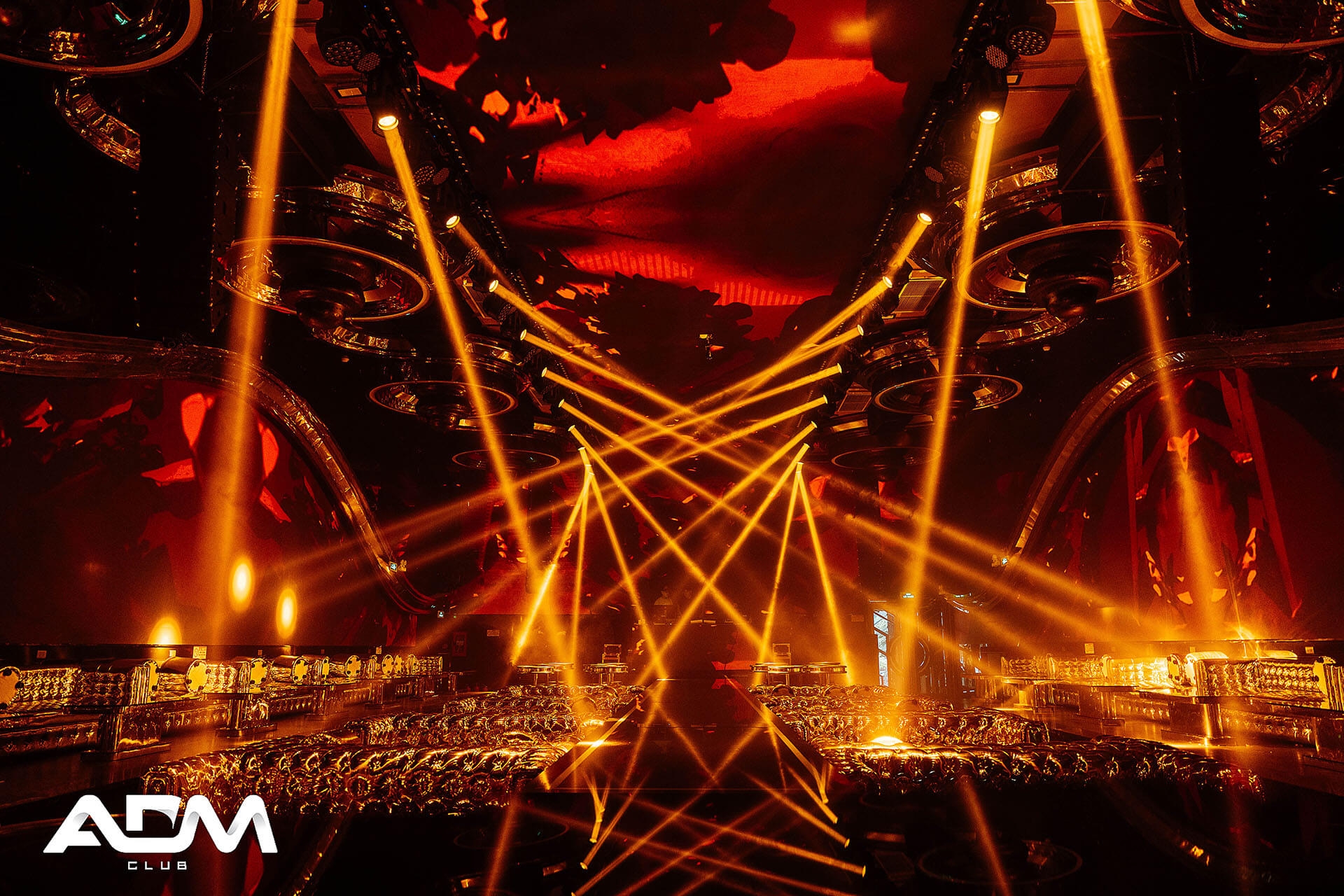 ADM Club interior with golden laser beams criss-crossing under a red ceiling above the dance floor