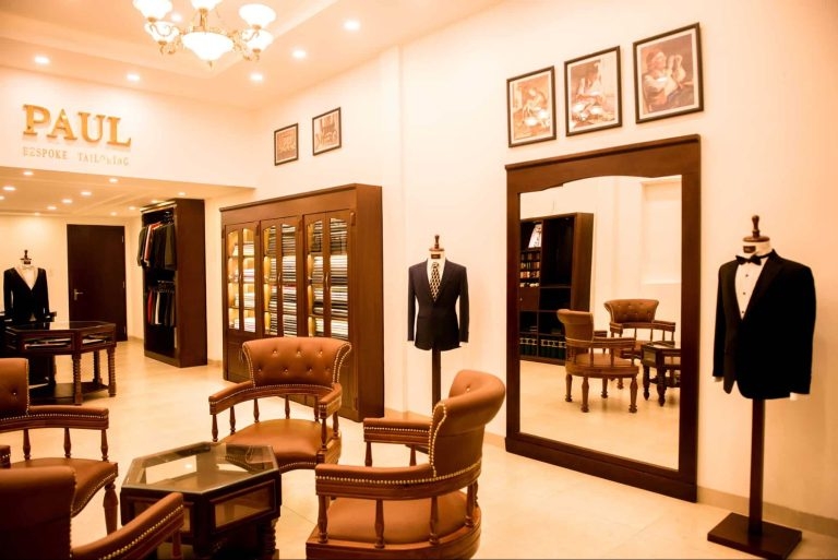 Paul Bespoke Tailor showroom interior with suits on mannequins, leather armchairs and a large standing mirror under a chandelier