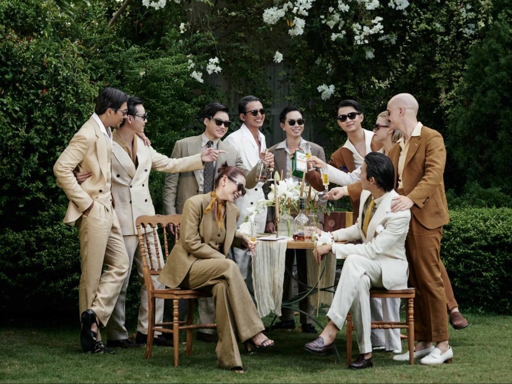 Group of stylish men and a woman wearing tan and cream tailored suits and sunglasses at an outdoor garden gathering