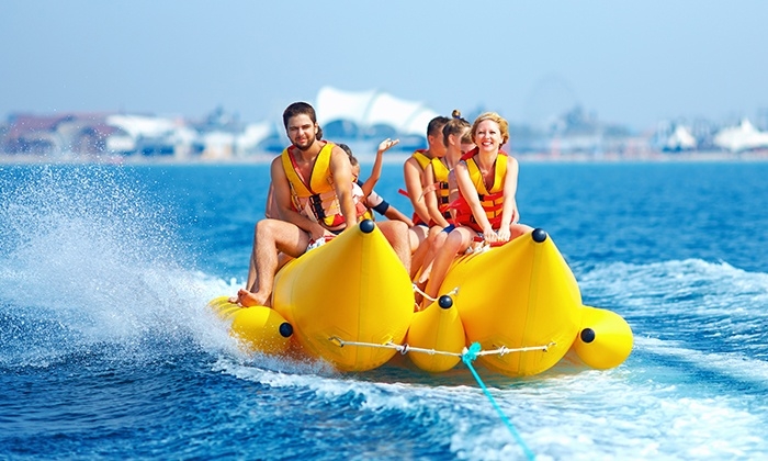 Group of smiling people in life jackets riding a yellow inflatable banana boat being towed across blue sea