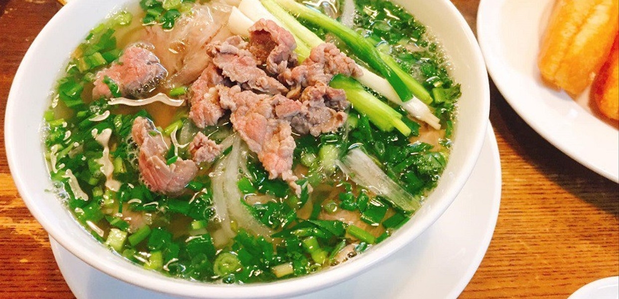 Hanoi-style beef pho bowl topped with sliced beef, onion and chopped scallions with fried dough alongside