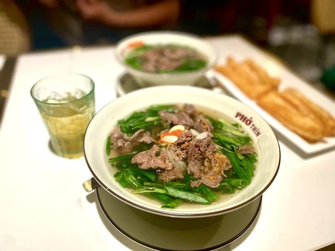 Pho Thin beef pho bowl with stir-fried beef and scallions, iced tea and fried dough on the table