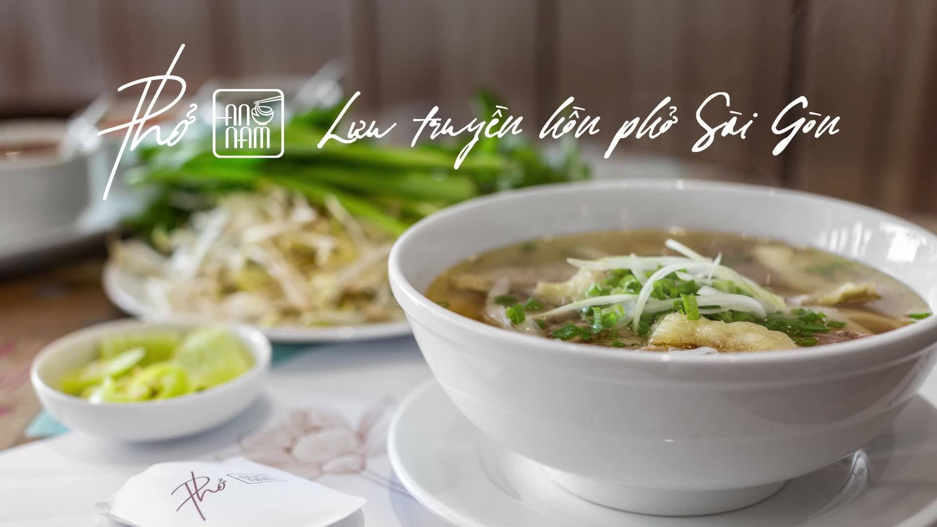 Pho An Nam white bowl of beef pho topped with scallions, served with a plate of herbs and pickled garnish