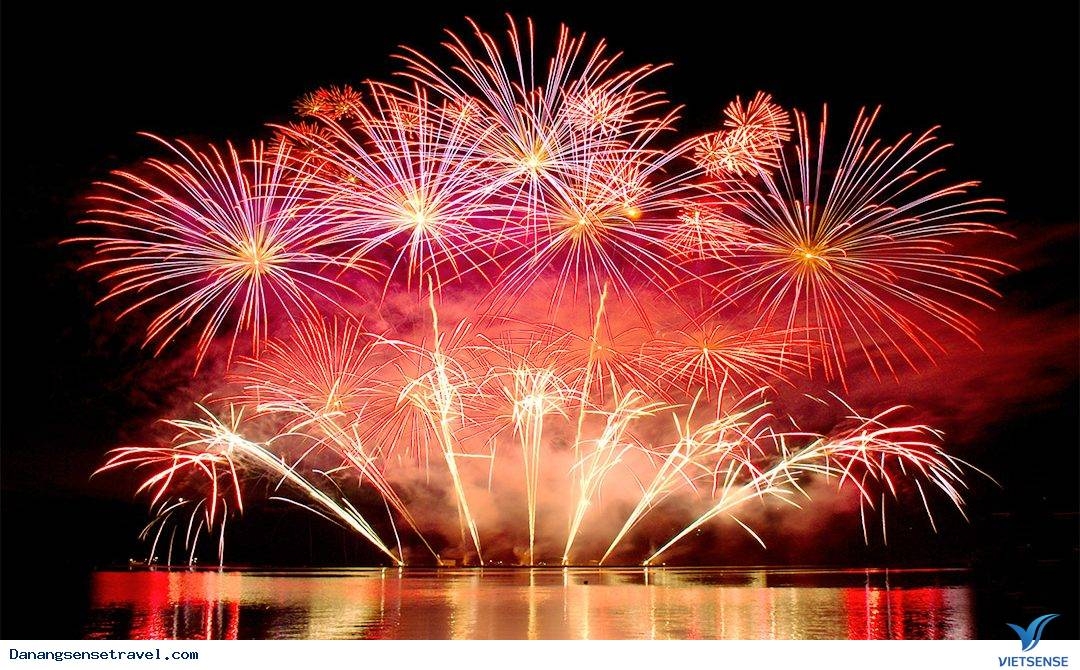 Red and gold fireworks bursting over water against a black night sky, reflected on the river surface
