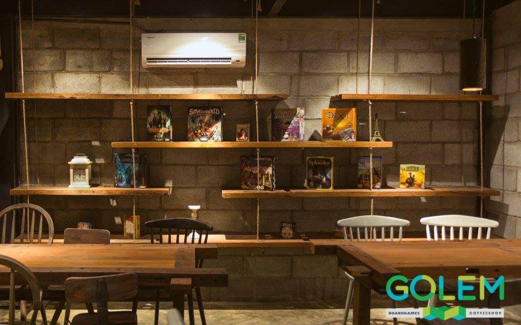 Golem coffee shop interior with board games on wooden wall shelves, exposed brick and wooden tables