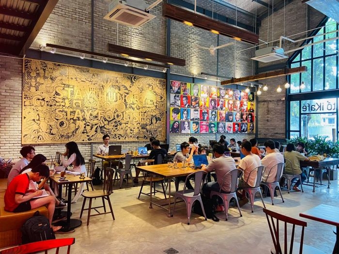 Busy iKafé with people studying at wooden tables, brick walls, mural art and Stay Hungry Stay Foolish sign