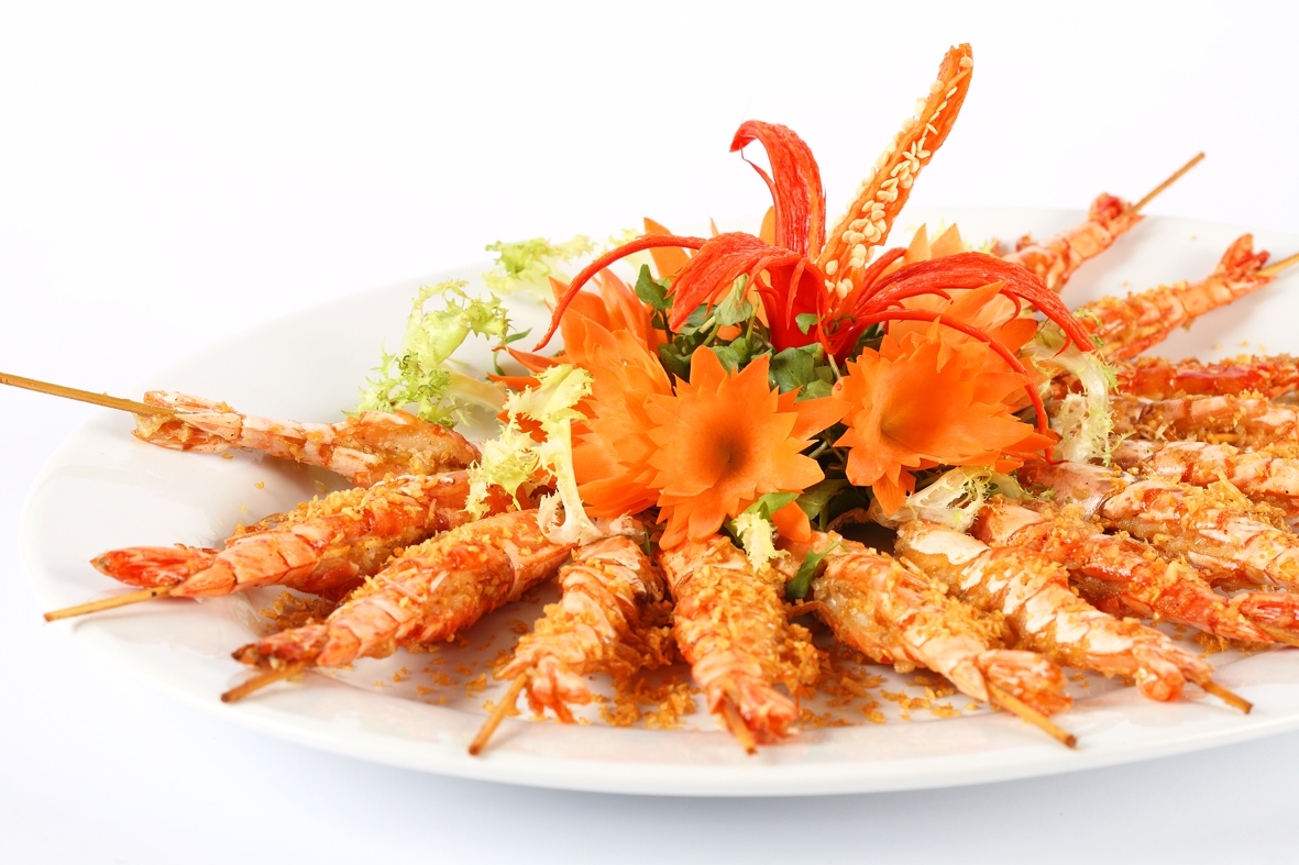 Plate of grilled prawn skewers arranged in a circle with carved carrot flower garnish