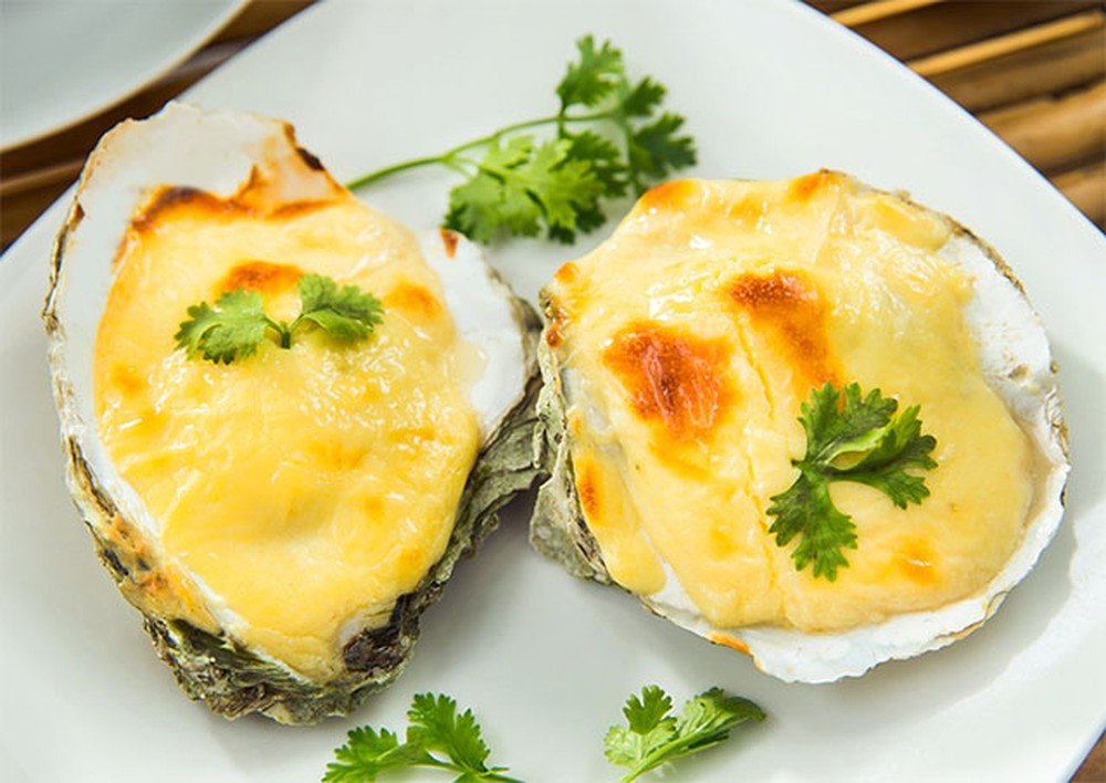 Two baked oysters topped with melted golden cheese and cilantro on a white plate