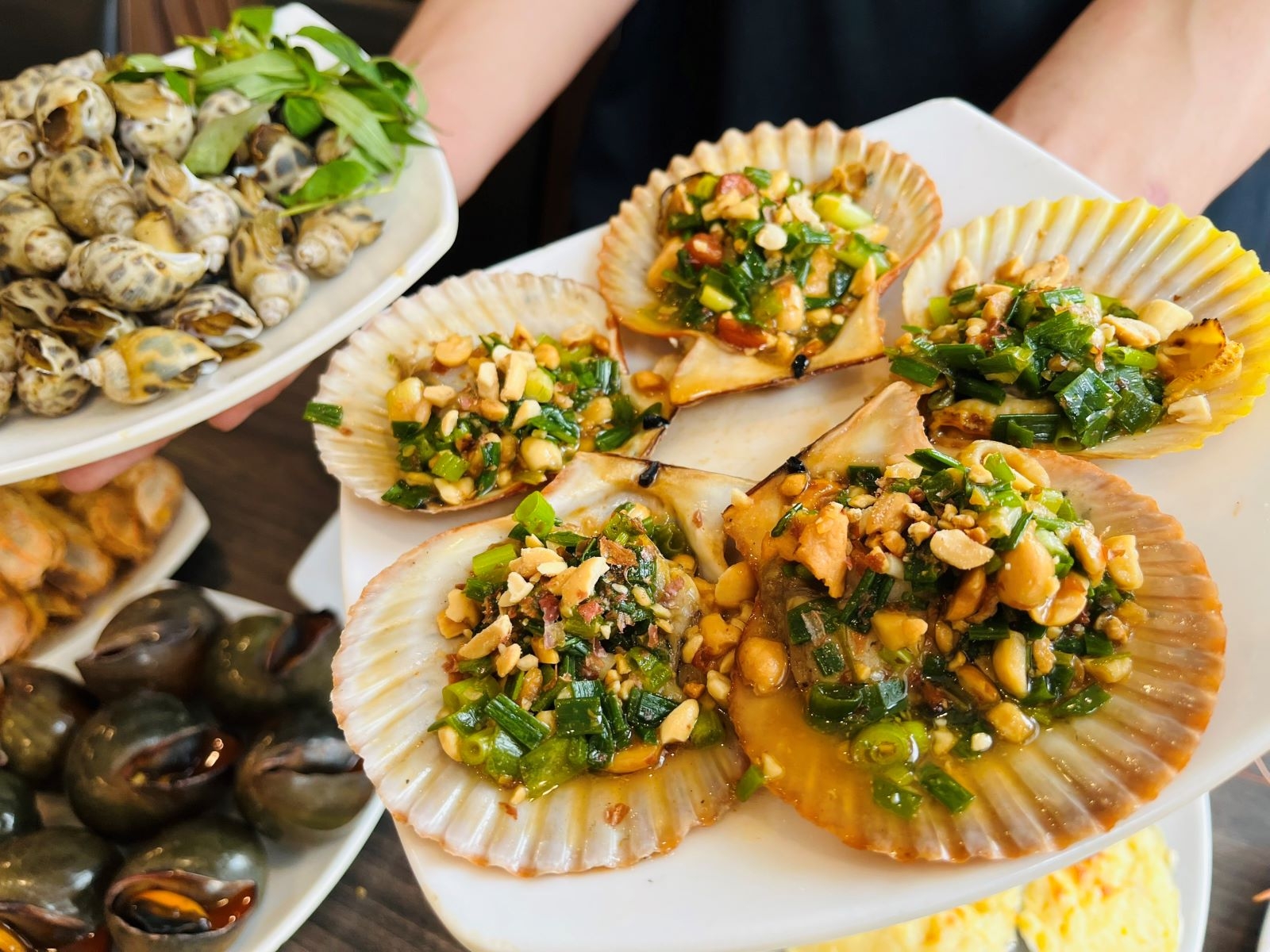 Grilled scallops topped with scallions and peanuts served with a plate of sea snails