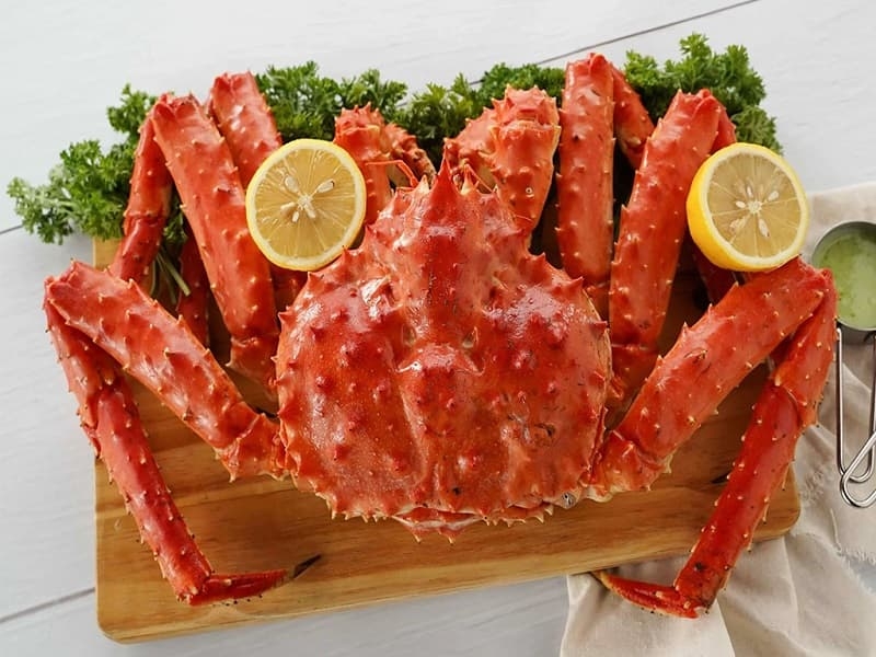 Whole steamed red king crab on a wooden board with lemon halves and parsley