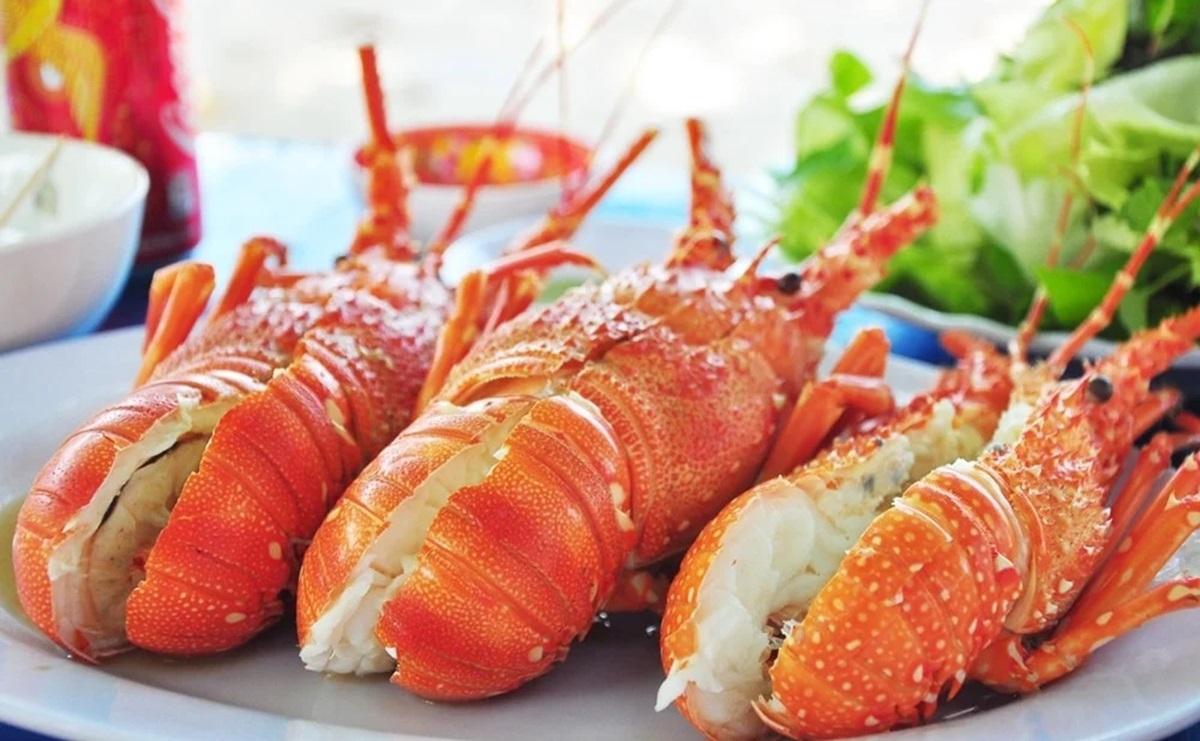 Halved grilled spiny lobsters showing white meat served on a plate with fresh herbs