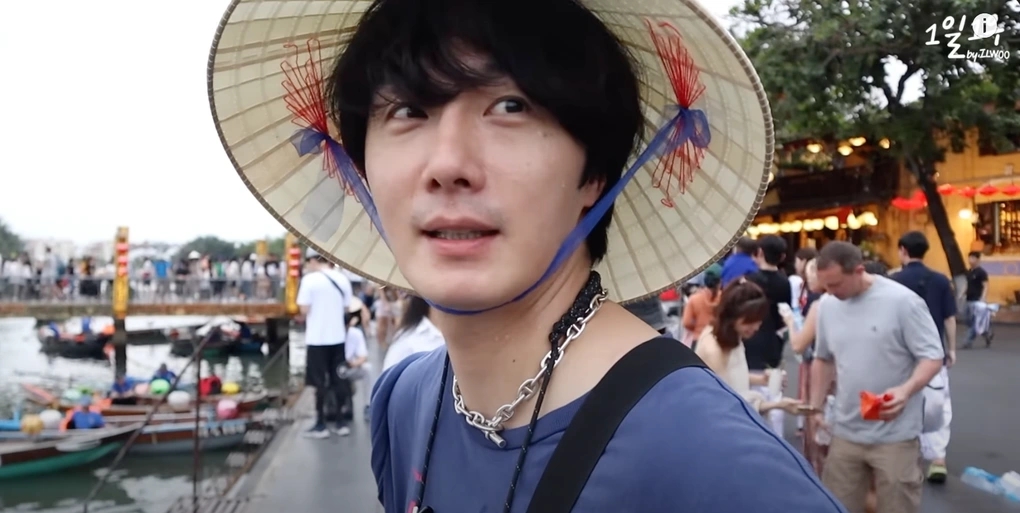 Korean tourist wearing a Vietnamese conical hat at Hoi An riverside with wooden boats and lantern-lit shops