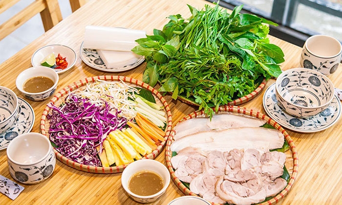 Vietnamese meal of sliced boiled pork, fresh herbs, vegetables, rice paper and dipping sauces on a wooden table