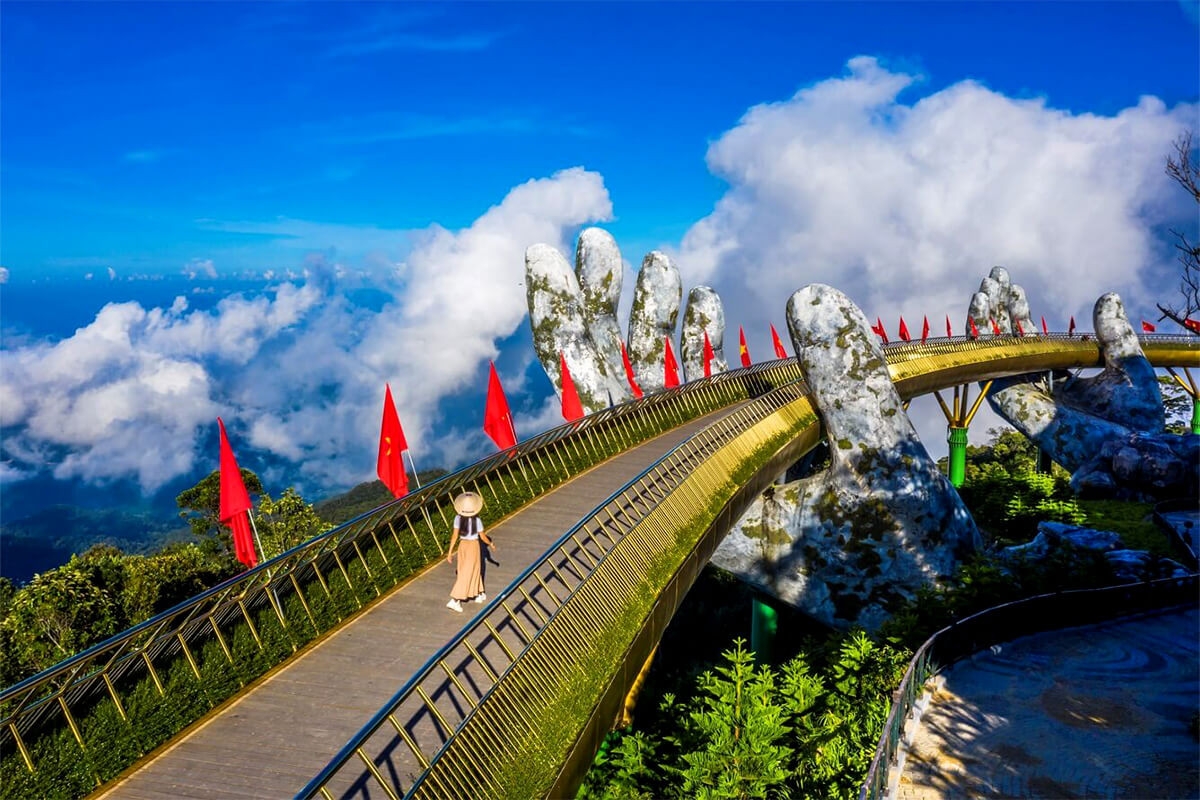 Golden Bridge held by giant stone hands at Ba Na Hills, lined with red flags above a sea of clouds