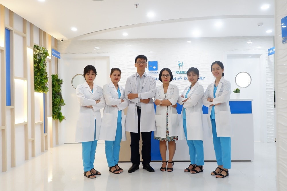 Six medical staff in white coats and blue scrubs standing together in a bright modern clinic lobby