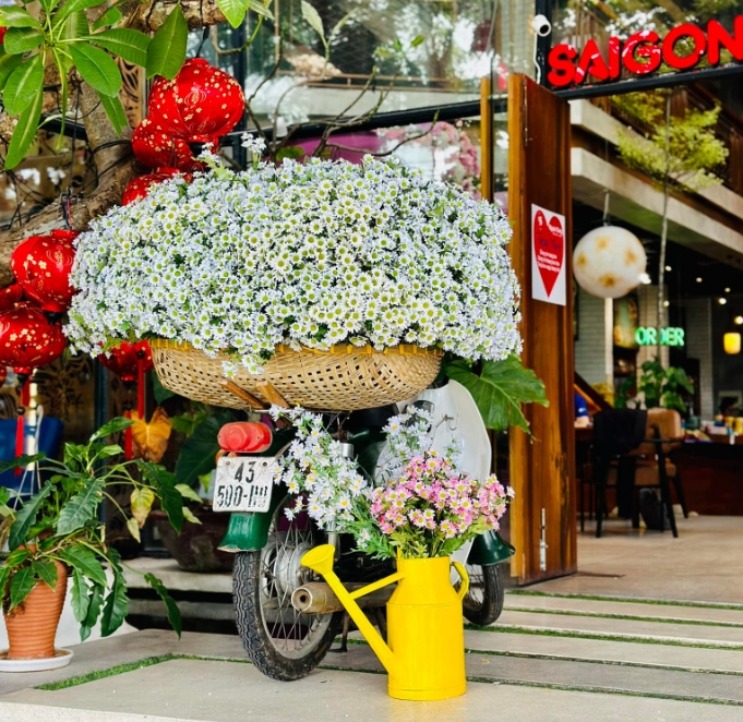 Motorbike loaded with a large basket of white daisies parked outside a cafe with a red Saigon sign and red lanterns