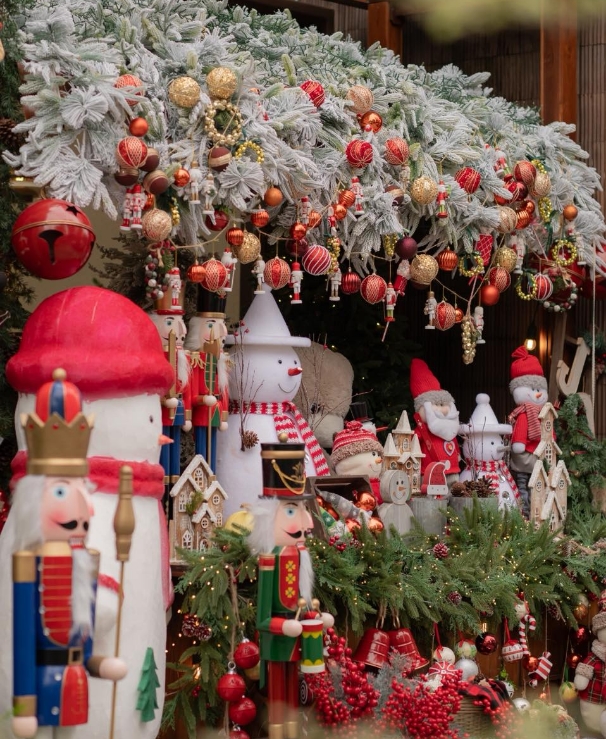 Christmas display of wooden nutcracker figures, snowmen, Santa statues and red and gold baubles under a snowy pine branch