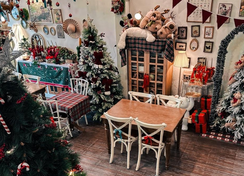 Cozy cafe interior with snow-dusted Christmas trees, plush reindeer toys, wrapped gifts and a wooden table with cream chairs